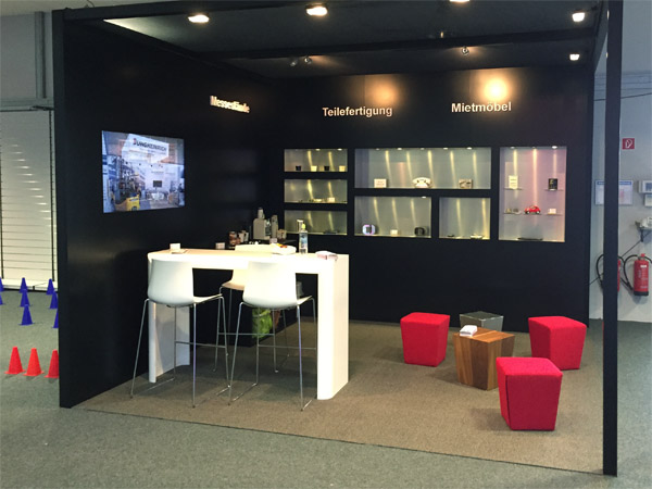 Messestand mit Einbauregalen, Br�ckentisch, Loungehocker, Beleuchtung
gefr�sten Logos und eingebautem Display